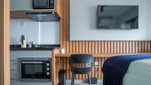 A compact kitchen with a microwave, oven, and a wooden countertop. - Furnished Studio in São Paulo with City Views (São Paulo)