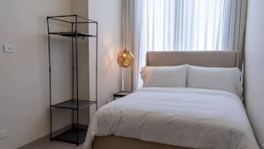 Une chambre à coucher avec un lit, une haute étagère en métal noir, une lampe de chevet et une fenêtre avec des rideaux.