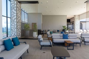 A spacious, modern lounge area with sofas, armchairs, and a coffee table, featuring large windows and a city view. - Condo Suite 2BR With View (Panamá)