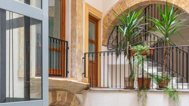 Un intérieur à plusieurs niveaux, agrémenté d’une arche en pierre, d’un balcon orné de plantes en pot et d’un escalier.
