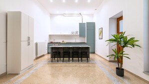 Une cuisine moderne avec un sol en marbre, un îlot central doté de chaises et une plante en pot.