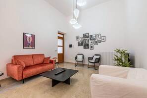 Uma sala de estar com um sofá vermelho, uma mesa de centro preta, duas cadeiras pretas, um sofá branco e uma parede com quadros.