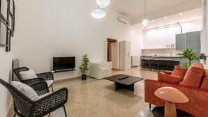 Un salon moderne doté d’un téléviseur à écran plat, de fauteuils en osier noir, d’un canapé rouge, d’une table basse et d’un coin cuisine avec des tabourets de bar.
