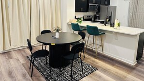Eine moderne Küche mit dunklen Schränken, einer weißen Arbeitsplatte und einem Essbereich mit rundem Tisch und Stühlen.