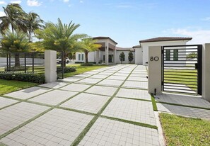 Een omheind woongebied met een verharde wandelpad, palmbomen en moderne huizen.