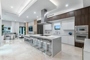 A modern kitchen with a central island, stainless steel appliances, and a dining area with bar stools. - Luxury Meets Miami (Miami)