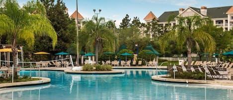 A pool area with lounge chairs and umbrellas, surrounded by palm trees and buildings.