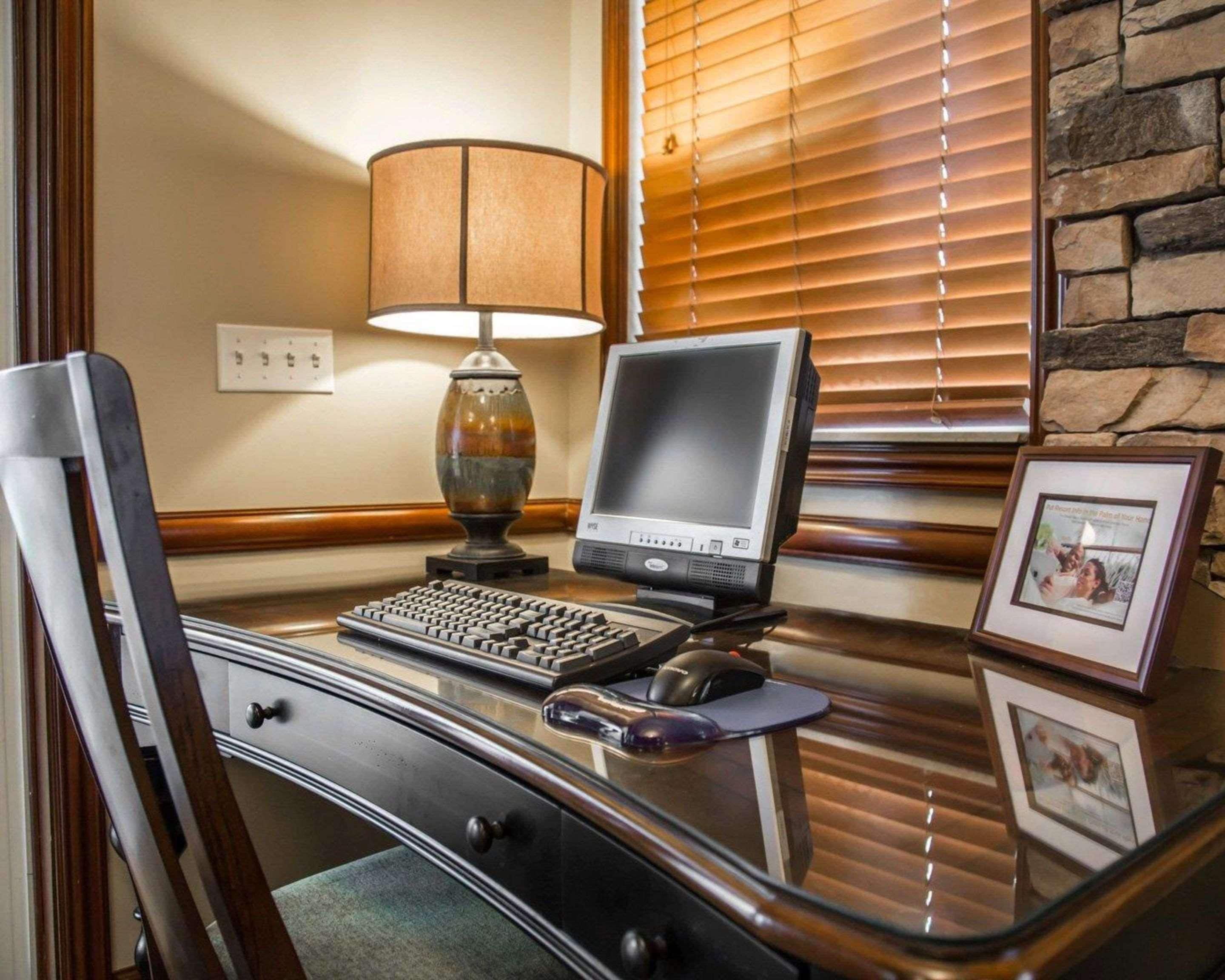 A computer desk with a desktop computer, keyboard, and mouse. There is a lamp, a framed picture, and a chair.