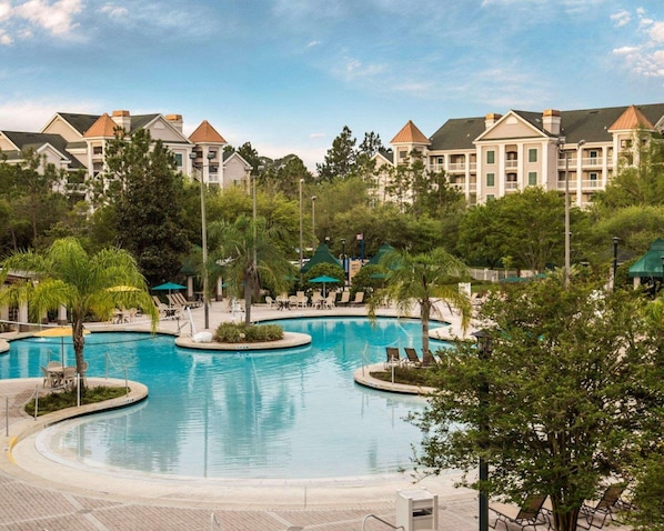 A swimming pool with lounge chairs and umbrellas, surrounded by trees and buildings with a uniform architectural style. - Hilton Vacation Club St. Augustine (St. Augustine)