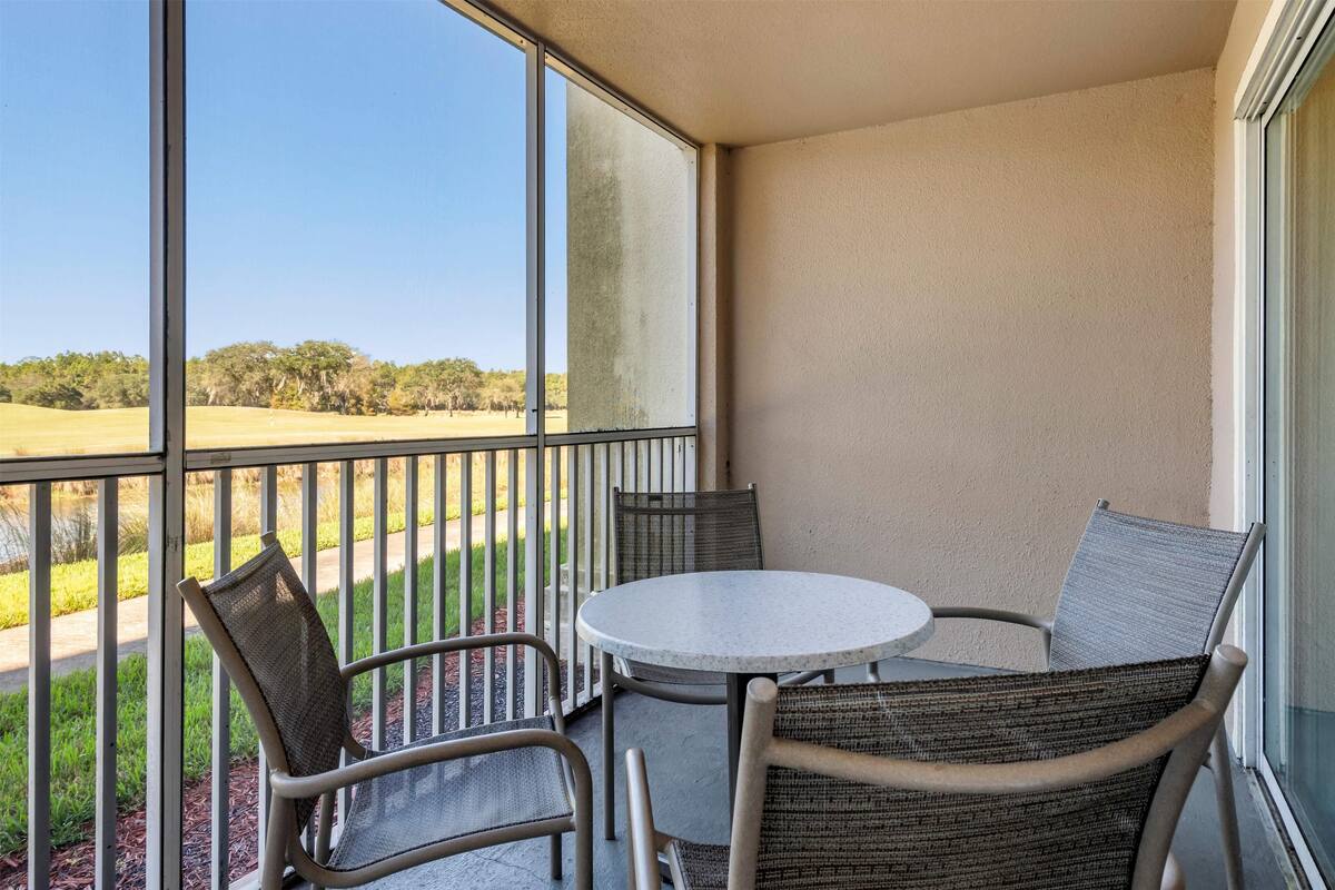 Un balcon avec une table ronde et des chaises en osier, donnant sur un terrain de golf.