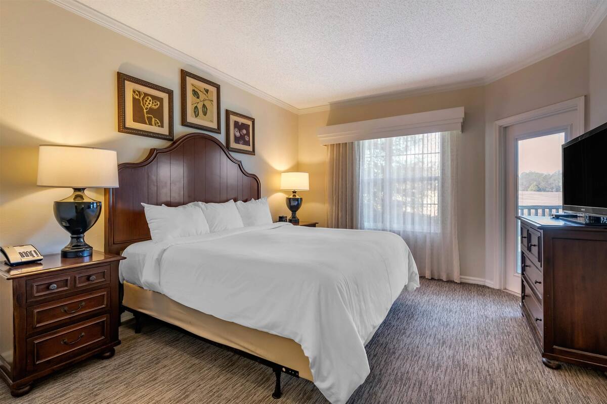 Une chambre d’hôtel avec un grand lit, deux tables de chevet avec des lampes, une télévision et une fenêtre avec des rideaux.