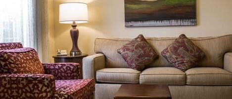 A living room with a sofa, patterned armchairs, a table, a lamp, and a painting on the wall.