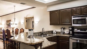 A kitchen with granite countertops, stainless steel appliances, wooden cabinets, a dining area with chairs, and a chandelier. - Hilton Vacation Club St. Augustine (St. Augustine)