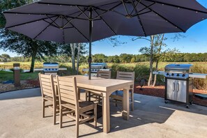 Eine Terrasse im Freien mit Tisch, Stühlen, einem großen Sonnenschirm und zwei Grillanlagen.