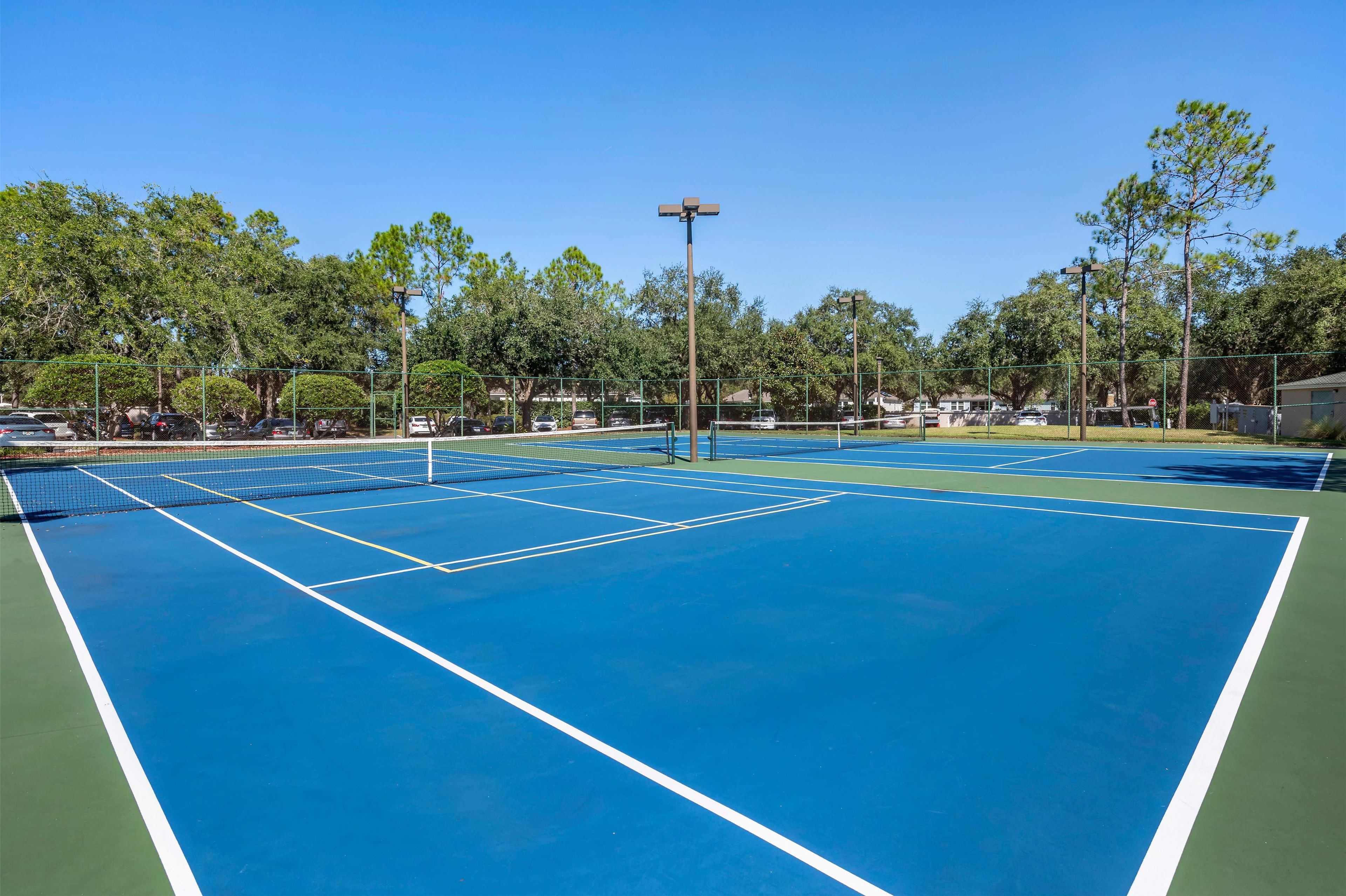 A tennis court with a net, surrounded by trees and a fence.