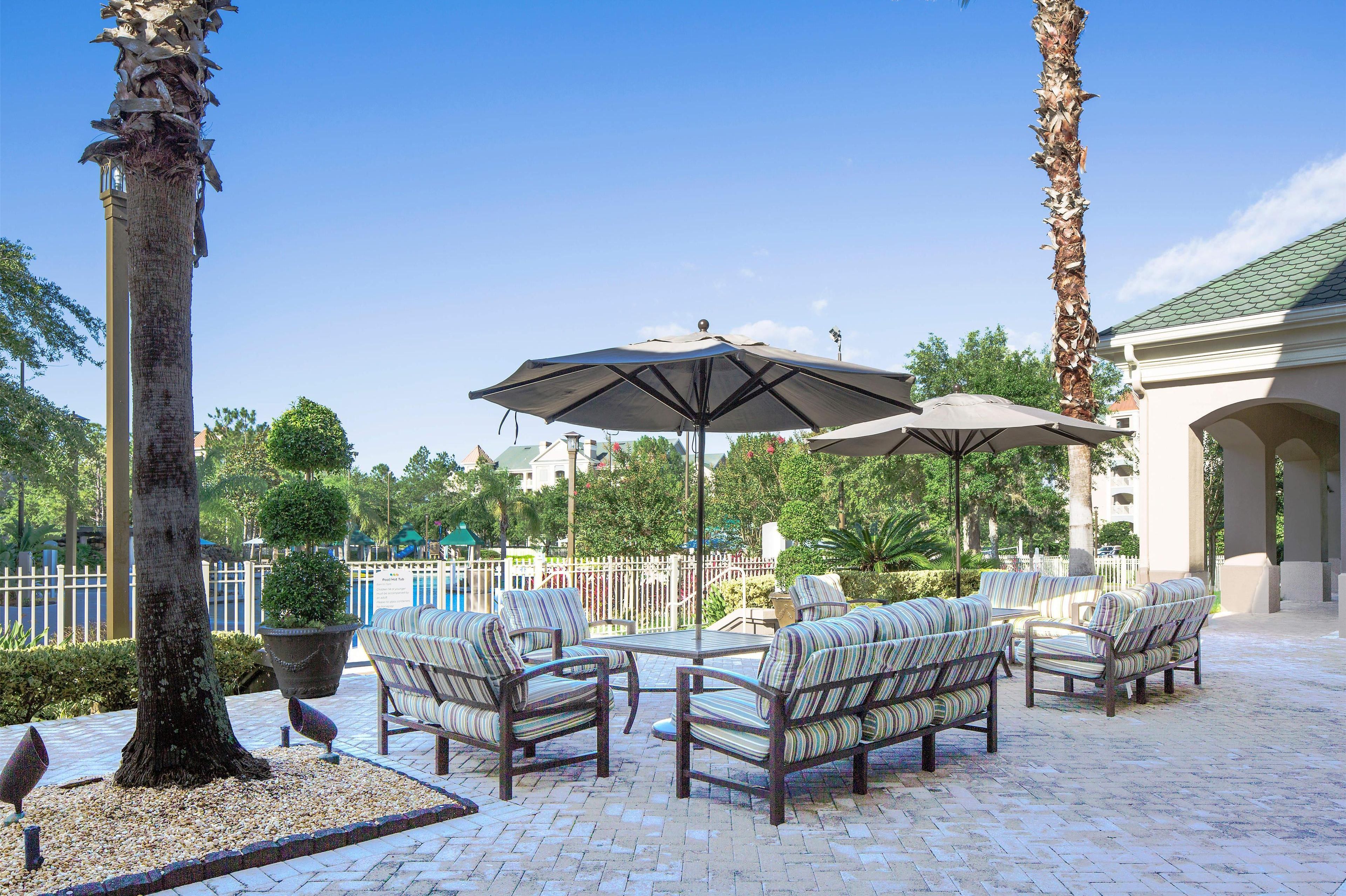 A patio area with outdoor furniture, umbrellas, and a pool in the background.