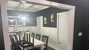 Une salle à manger avec une table blanche et des chaises en bois foncé, un lustre et des appliques murales décoratives.