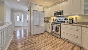 Una cocina con gabinetes blancos, un refrigerador de acero inoxidable, un microondas, una estufa y una cafetera.