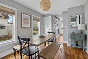 A dining area with a wooden table, black chairs, a woven ceiling light, and a staircase leading to another room. - Charming Home with Hot tub & walk to town! (Three Oaks)