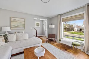 Ein modernes Wohnzimmer mit einer Couch, einem Couchtisch, einem Sessel, einer Lampe und Blick ins Freie.