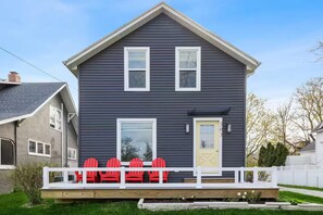 A two-story house with a front porch, a yellow door, and a number '303' on the door. - Charming Home with Hot tub & walk to town! (Three Oaks)