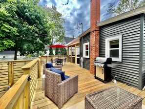 Eine Terrasse mit Korbmöbeln, einem Grill und einem roten Sonnenschirm.