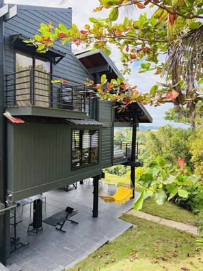 Ein modernes Haus mit einem Balkon, Trainingsgeräten im Freien und Blick auf die Landschaft.
