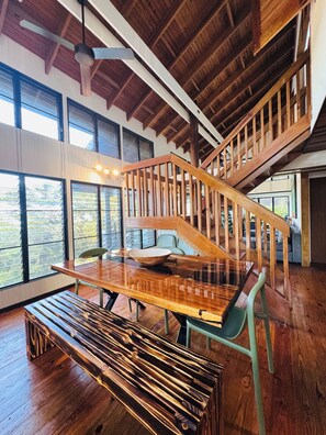 Ein geräumiger Raum mit einer Holztreppe, großen Fenstern und einem Essbereich mit Holztisch und Bänken.