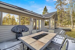 A covered outdoor dining area with a table and chairs, a barbecue grill, and a view of trees and a house. - AC, View of Golf Course, Ping Pong, by North Store (Sunriver)