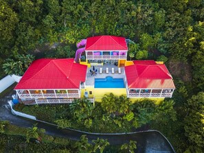 A large, two-story building with a red roof, a swimming pool, and a white fence surrounding the property.
