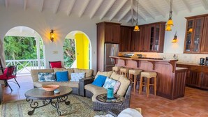 A spacious living area with wicker furniture, a kitchen with wooden cabinets, and a balcony with a view of greenery.