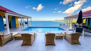 A poolside area with lounge chairs, a pool, and a view of the sea.