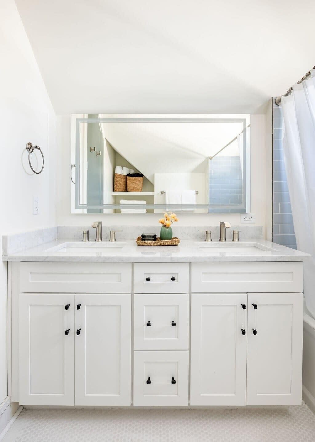 Een badkamer met een groot wit wastafelmeubel, een spiegel en uitzicht op een inloopkast met manden en handdoeken.