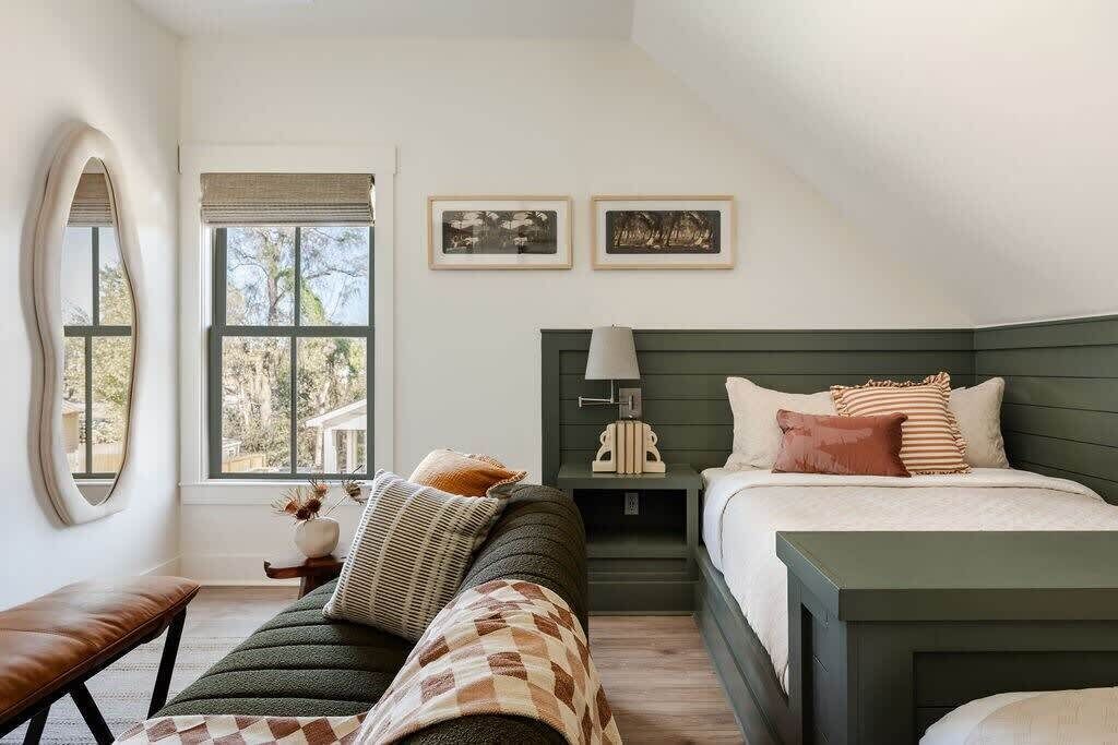 Une chambre à coucher avec un lit, un banc, une fenêtre et deux tableaux encadrés accrochés au mur.