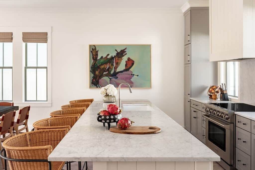 Een moderne keuken met een centraal eiland, een eethoek met rieten stoelen en een groot raam.