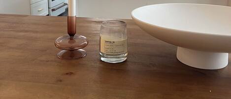A kitchen with white cabinets, a white countertop, a hanging light, and a wooden table with a candle and a glass of water.
