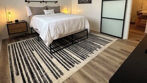 A bedroom with a bed, bedside tables, a ceiling fan, a wall-mounted air conditioner, a black-framed sliding door, and a striped rug. - Cozy 1-bedroom condo in enjoyable Chico with AC (Chico)