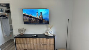 A modern living room with a flat-screen TV mounted on the wall, a wooden cabinet with a woven design, and a small decorative vase on the cabinet. - Cozy 1-bedroom condo in enjoyable Chico with AC (Chico)