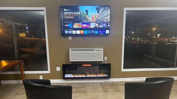 Een woonkamer met een flatscreen televisie aan de muur, een open haard en twee zwarte fauteuils.