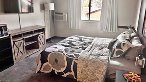Een hotelkamer met een bed, een televisie, een bureau, een lamp, een raam met gordijnen en een vaas met bloemen.