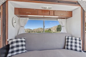A cozy RV interior with a large bed, a clock, and a view of a mountainous landscape. - Pet-friendly RV stay at a horse ranch in a fenced 5 acre lot in the hills (Acton)
