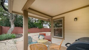 A covered patio with outdoor furniture, a grill, and a view of a red fence and trees. - Bulverde Vacation Home (San Antonio)