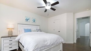 A bedroom with a bed, nightstand, lamp, ceiling fan, and artwork on the wall. - Bulverde Vacation Home (San Antonio)