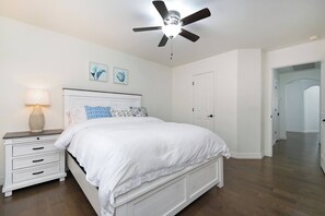 A bedroom with a bed, nightstand, lamp, ceiling fan, and artwork on the wall. - Bulverde Vacation Home (San Antonio)