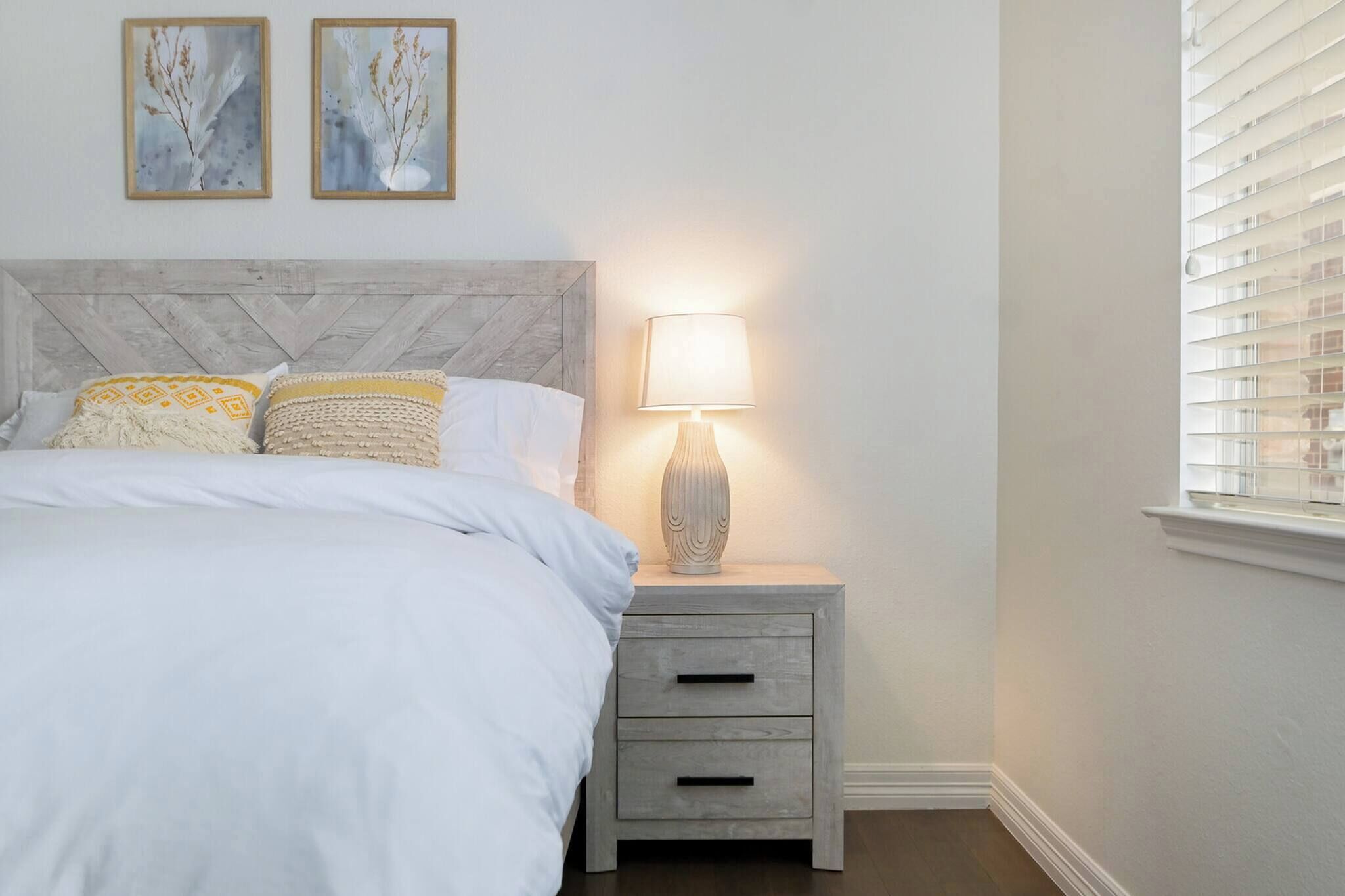 A bedroom with a bed, nightstand, lamp, and two wall-mounted pictures.