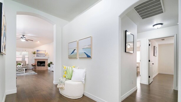 A spacious hallway with wooden flooring, white walls, and a fireplace. There are framed pictures on the wall and a white bench with cushions. - Bulverde Vacation Home (San Antonio)