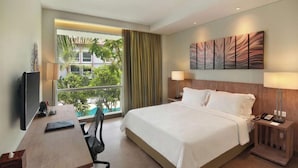 A hotel room with a bed, desk, chair, TV, and a window with a view of greenery. - PALMERAS DEL CARIBE - STUDIOS and SUITES (Punta Cana)