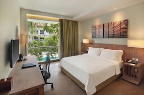 Ein Hotelzimmer mit Bett, Schreibtisch, Stuhl, Fernseher und einem Fenster mit Blick ins Grüne.