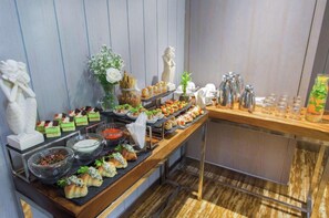 A buffet setup with various food items, a statue, and a vase of flowers. - PALMERAS DEL CARIBE - STUDIOS and SUITES (Punta Cana)