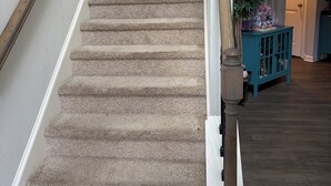 Una escalera con alfombra, barandilla de madera, un mueble azul aguamarina y una planta en maceta.